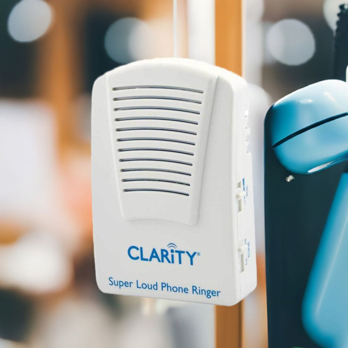 Clarity Super Loud Phone Ringer device mounted beside an analog telephone with a blurred background. 