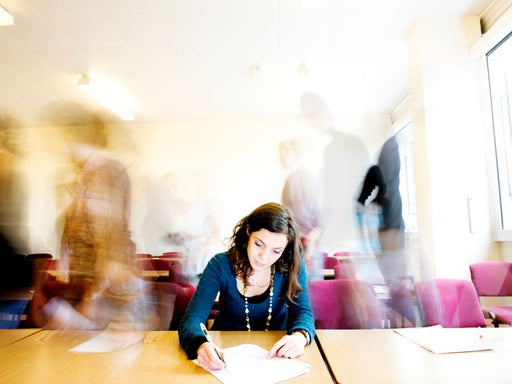 Woman writing at a table with blurred people in the background