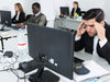 Stressed man at a desk with computer and colleagues in the background
