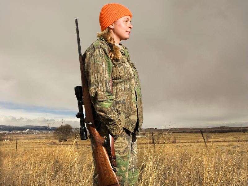 Serenity Choice Reusable Hearing Protection for HUNTING & SHOOTING Earplugs being used by a young woman dressed in an orange tuque and camouflage pants and jacket holding her rifle over her shoulder.  