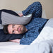 Man lays with a pillow over his ears in bed.  He would benefit from Serenity Choice Reusable Hearing Protection for SLEEP ear plugs. 