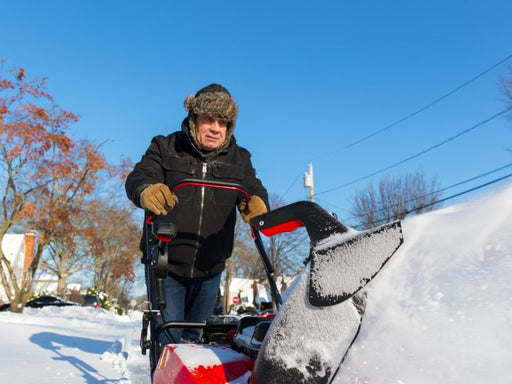 A person using a snow blower to clear snow from a sidewalk on a sunny winter day.