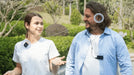  Two people walking outdoors, one speaking into the remote microphone and the other listening with earbuds on the Trihear Convo More Assistive Listening Device with Remote Microphone.