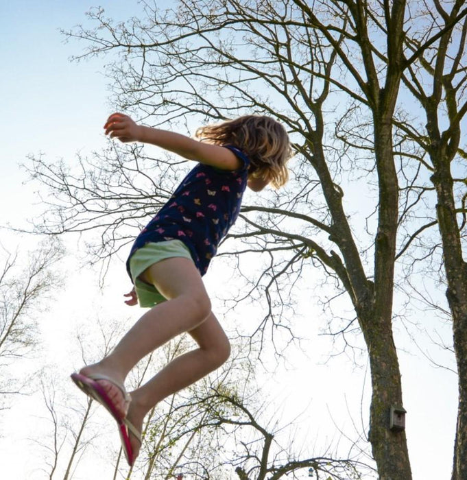 Active child wearing the Phonak Stick 'n' Stay Hearing Aid Stickers (30 pair) 098-0353.  Child jumping in the air with trees in the background. 